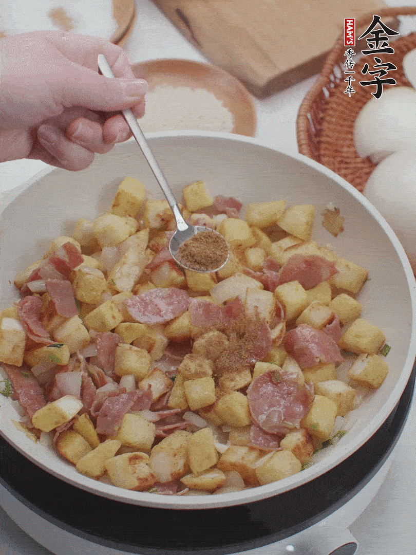 起鍋少油，煸香洋蔥丁、蔥白，加入金字培根火腿翻炒幾下，再加入饅頭丁、1小勺孜然粉、少許鹽翻炒均勻并鋪平。