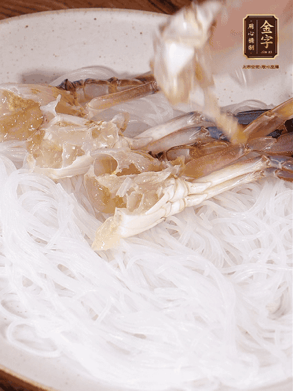 盤底墊上粉絲，擺上梭子蟹、火腿片，撒姜粒，淋上蒸魚豉油、花雕酒調(diào)味腌制15分鐘